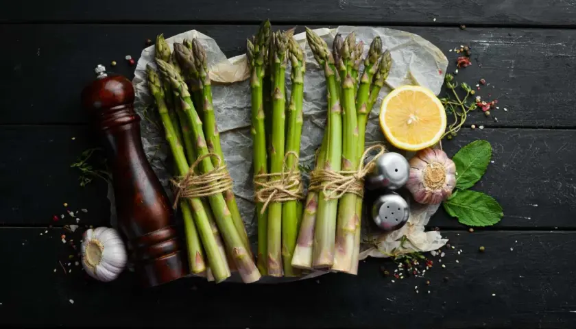 Des asperges fraîches, citron, ail et moulin à poivre sur fond noir. Idéal pour savoir quel vin avec asperges.