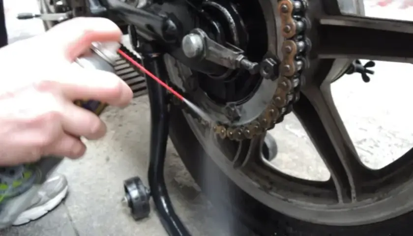 Mano spruzza spray sulla catena della moto per pulirla.