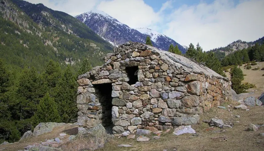 Antigua cabaña de piedra en el Vall de la Llosa, rodeada de pinos y montañas nevadas.
