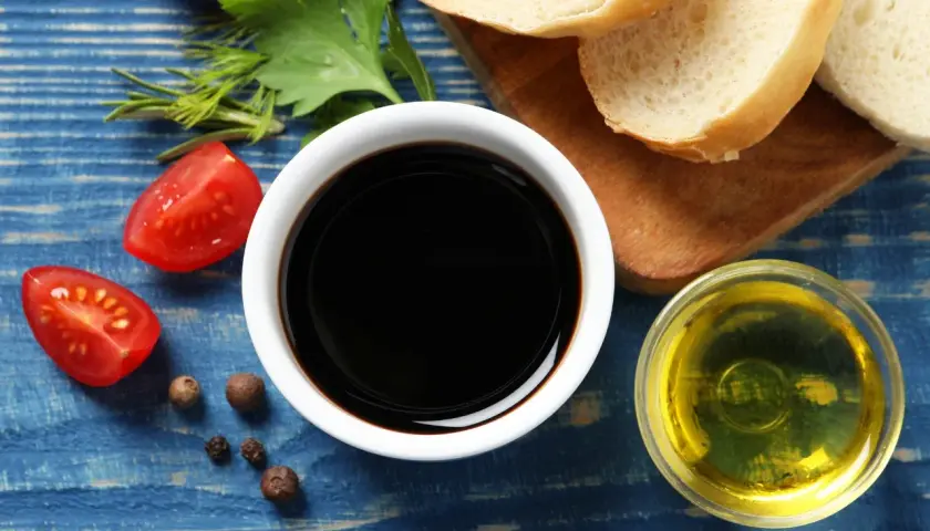 Sos do czego? Ocet balsamiczny, oliwa, pomidorki i pieprz na niebieskim tle. Idealne składniki na pyszną sałatkę.