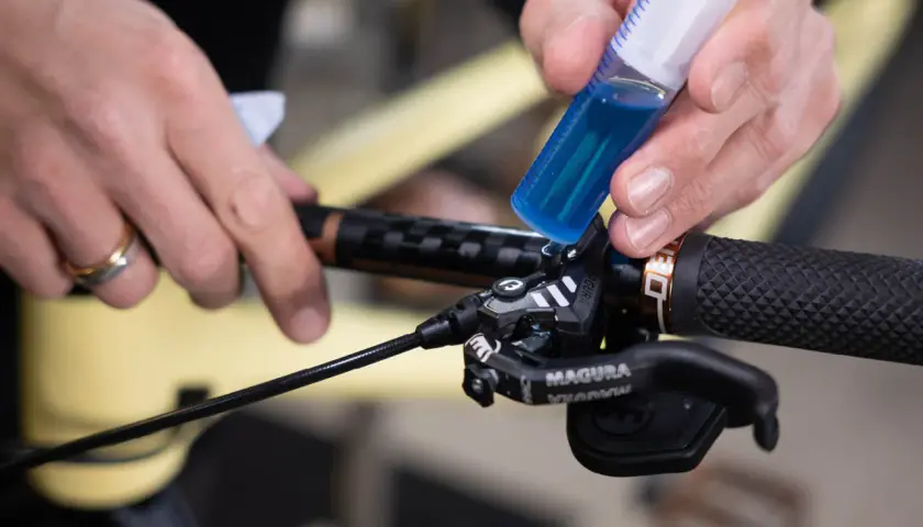 Hands add blue brake fluid from a syringe to a bicycle brake lever. This fluid is corrosive due to its hygroscopic nature, absorbing moisture.
