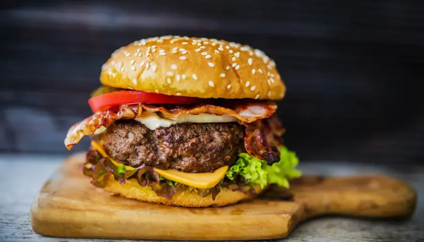 Soczysty burger z wołowiny z bekonem, serem, pomidorem i sałatą na desce.