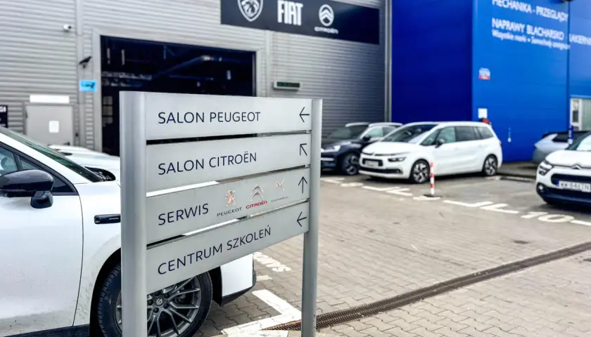 Znak z napisem "Salon Peugeot", "Salon Citroën", "Serwis" i "Centrum Szkoleń" przy salonie samochodowym. ASO skrót.