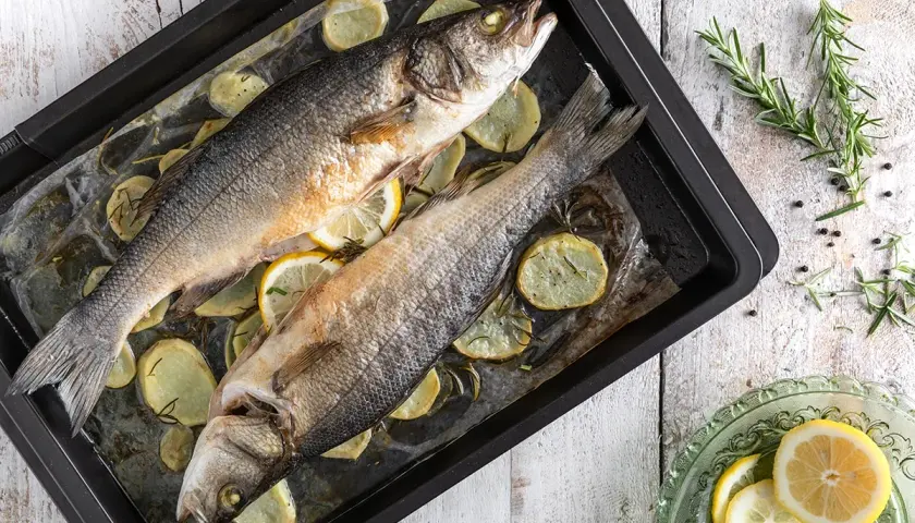 Due branzini al forno su teglia con patate, limone e rosmarino. Un piatto semplice e gustoso pronto per essere servito.