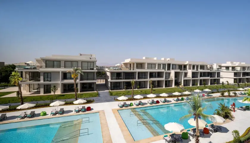 Nowoczesne budynki hotelowe Rixos z basenami i leżakami pod palmami.