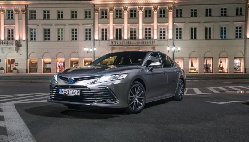 Elegancka, szara Toyota Camry 2024 zaparkowana nocą przed zabytkową kamienicą.