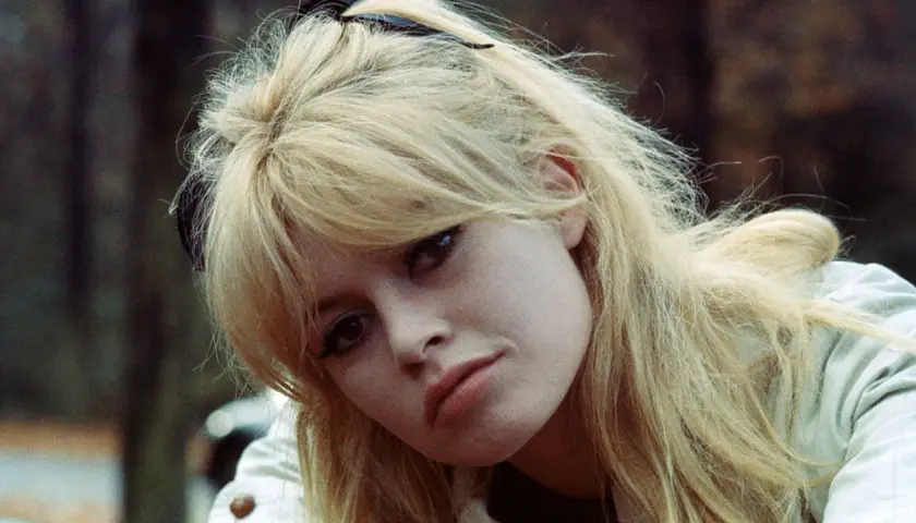 Blonde Frau mit langen Curtain Bangs, die leicht zerzaust sind. Ihr Blick ist nach unten gerichtet.