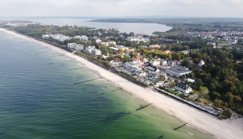 Widok z lotu ptaka na nadmorską miejscowość Mielno, z plażą, morzem i zabudowaniami. Ile mieszkańców ma Mielno? Tego nie widać, ale jest tu pięknie.