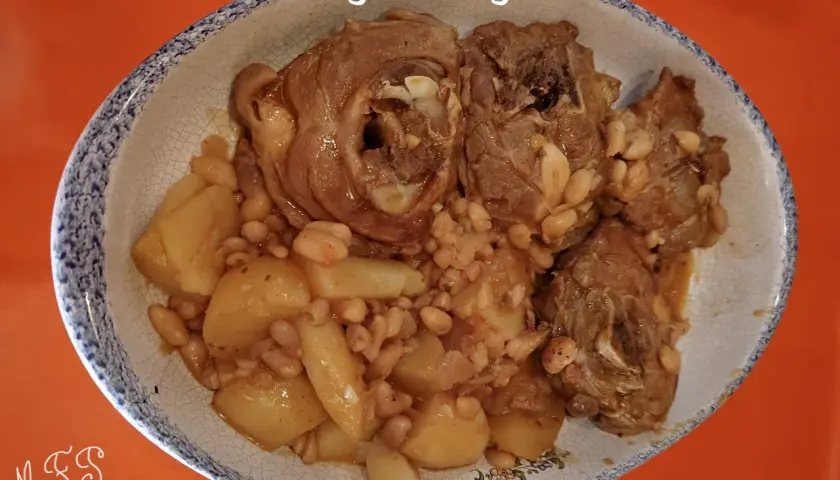 Un plat de ragout d'agneau avec des pommes de terre et des haricots blancs, servi dans un plat ovale à bordure bleue.