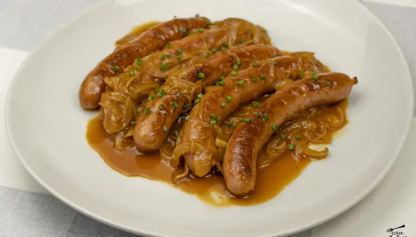 Salchichas doradas en salsa de cebolla caramelizada, un plato delicioso para aprender como hacer salchichas caseras.