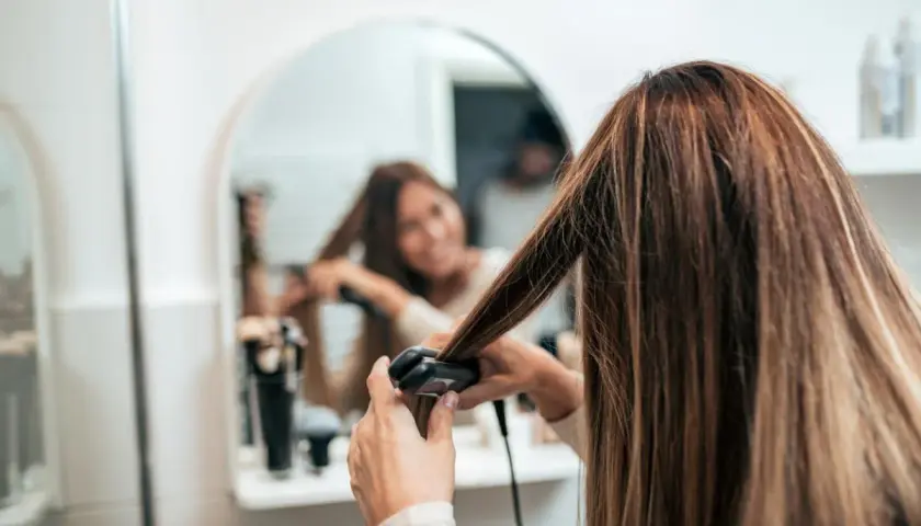 Mujer se alisa el pelo mojado frente al espejo.