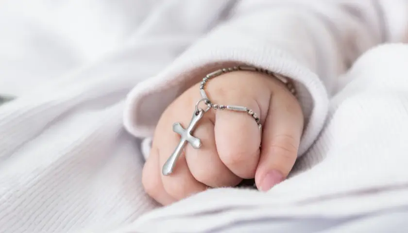 Dziecięca dłoń z krzyżykiem na nadgarstku. Zastanawiasz się, ile trwa msza z chrztem?