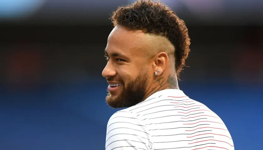 Sonrisa de Neymar con su característico peinado mohicano, luciendo una camiseta a rayas blancas y rojas.