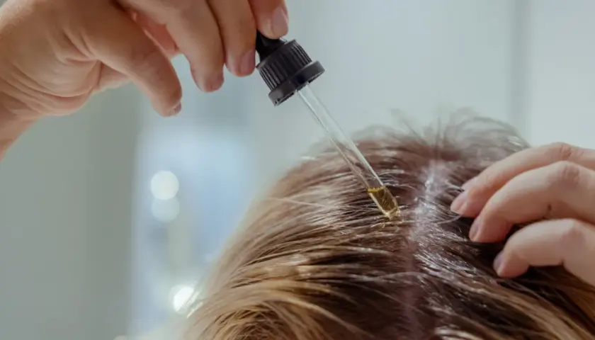 Kropla olejku z witaminą PP aplikowana pipetką na skórę głowy.