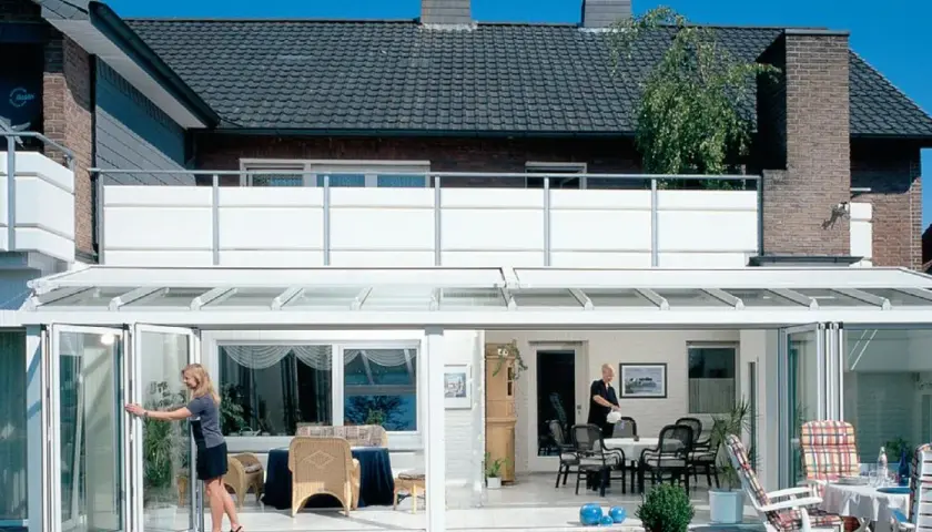 Nowoczesny balkon dostawny do domu jednorodzinnego, z przeszklonym ogrodem zimowym i składanymi drzwiami.