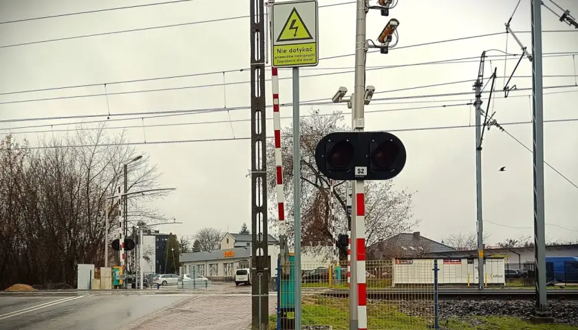 Kamery na przejazdach kolejowych monitorują bezpieczeństwo. Na zdjęciu widać sygnalizację świetlną, rogatki i kamery nadzorujące.