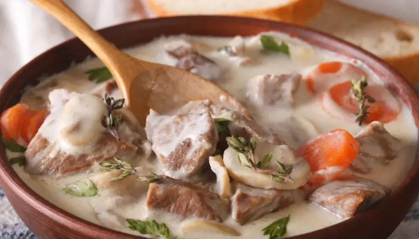 Un réconfortant blanquette de veau facile, servi dans un bol en bois avec une cuillère, garni de persil et de thym.