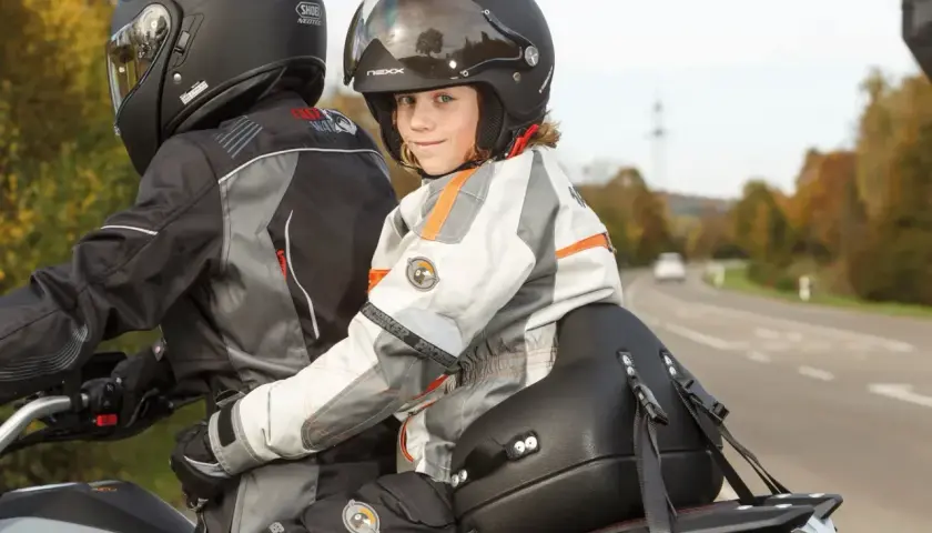 Dziecko w kasku z uśmiechem siedzi z przodu motocykla, gotowe na wspólną podróż. Przewożenie dziecka na motocyklu to przygoda!