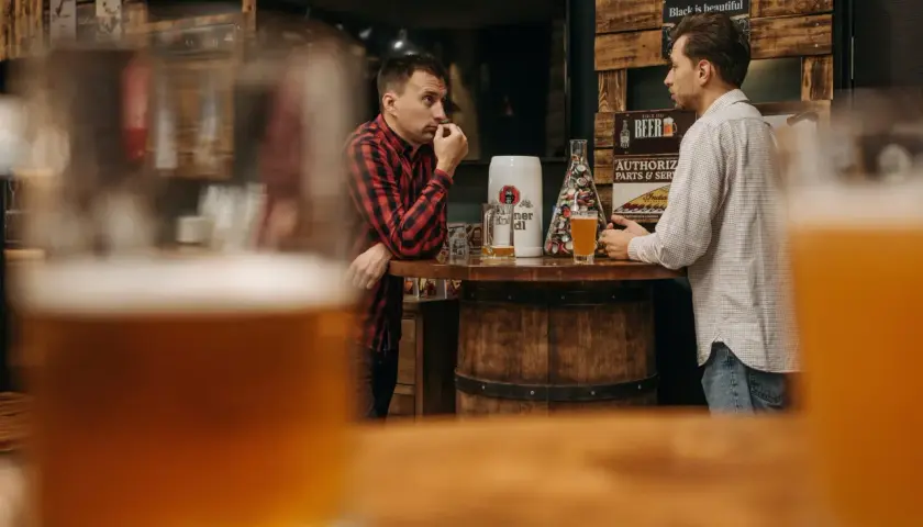 Dwóch mężczyzn rozmawia przy barze. Na blacie stoi kufel i szklanka piwa. Ciekawe, ile schodzi jedno piwo w takim miejscu.