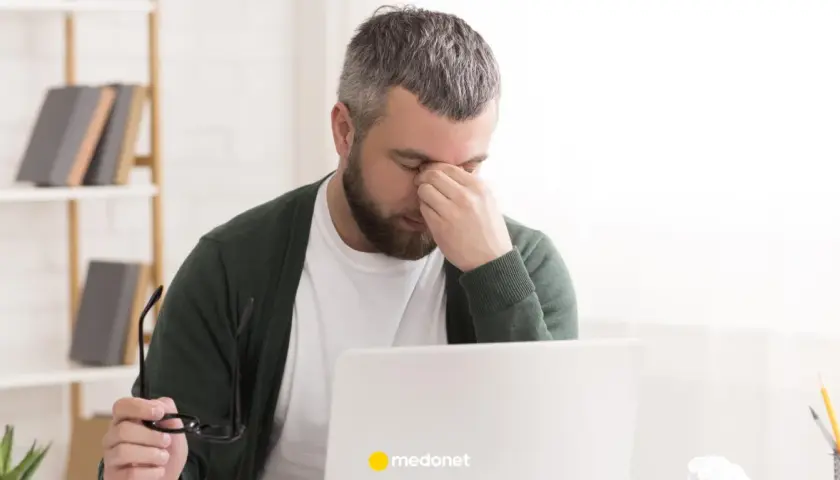 Mężczyzna z zespołem pustego siodła masuje oczy, siedząc przy laptopie.
