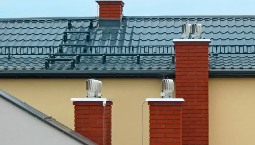 Dwa ceglane kominy z obrotowymi nasadami zapewniają sprawną wentylację w domu.