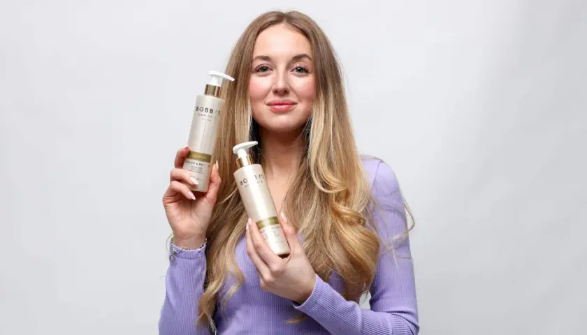 En kvinna med långt, blont hår håller upp två flaskor från Bobb's Hair Care. Hon har tunt hår och hoppas på att dessa produkter ska hjälpa.