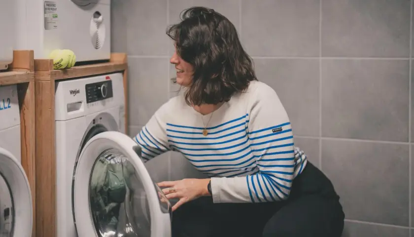 Kobieta w paski wkłada ubrania do pralki. Dowiedz się, jak prać odzież termoaktywną, by służyła latami.