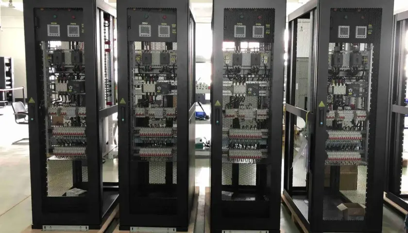 Cuatro racks negros con equipos electrónicos visibles a través de rejillas, parte de un cuarto de comunicaciones.
