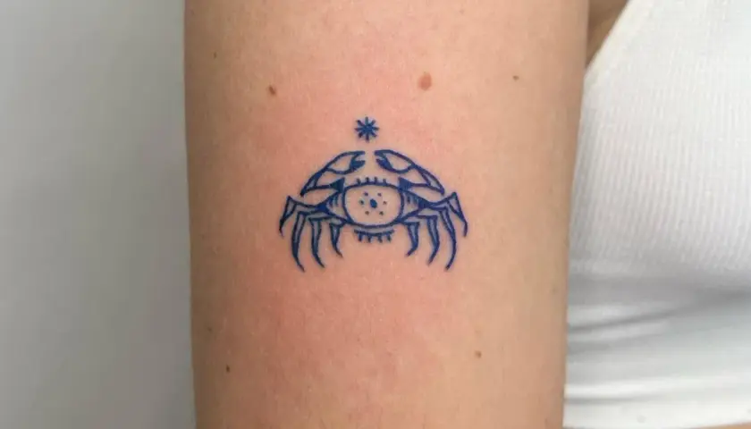 Niebieski tatuaż raka z okiem w środku, symbolizujący intuicję i ochronę.