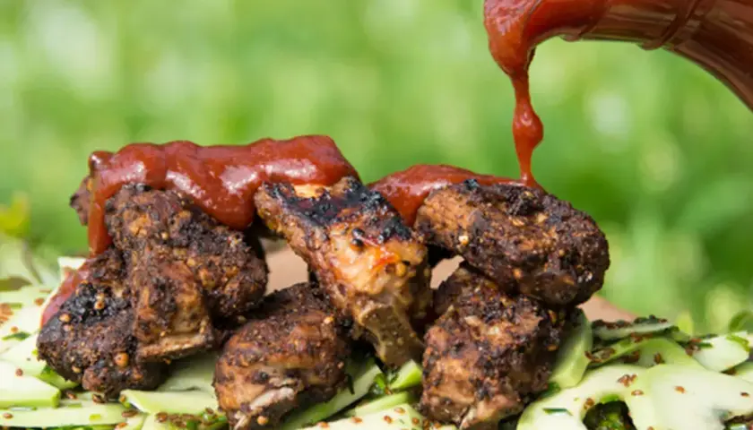 Grillade revbensspjäll toppas med en generös mängd röd bbq sås, serverade på en bädd av gurksallad.