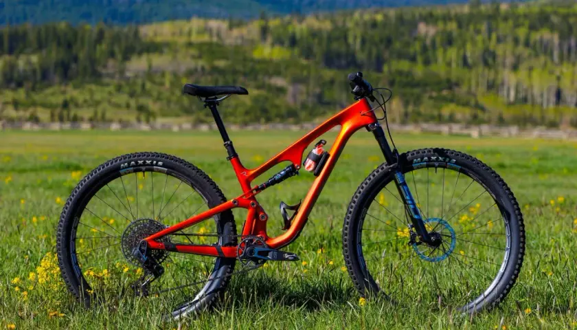 An orange Revel Ranger V2 mountain bike sits in a grassy field, ready for adventure. This revel ranger v2 review shows its sleek design.