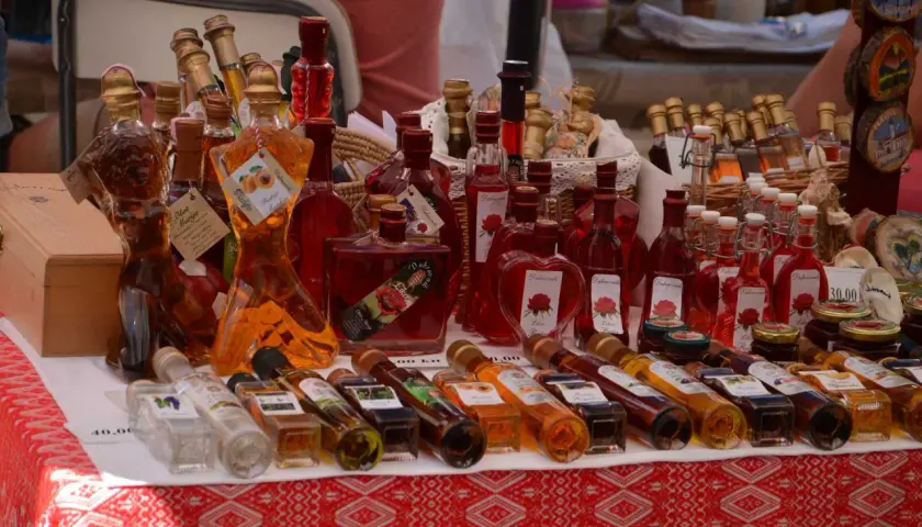 Różnorodne butelki z rakiją, w tym te w kształcie kobiecym, oferowane na targu. Co to rakija? To tradycyjny alkohol, często owocowy.