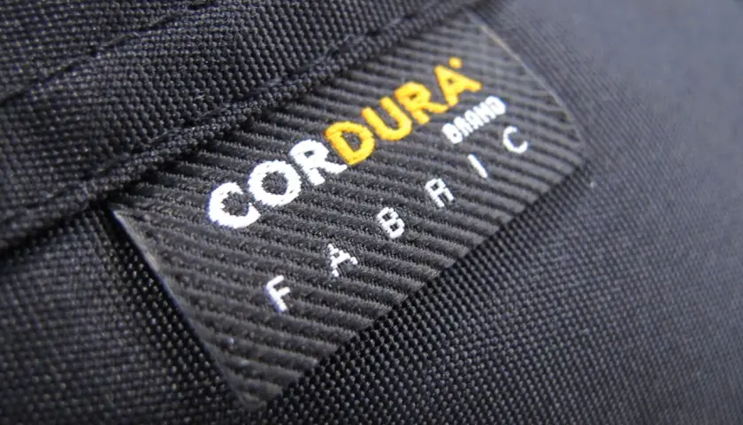 Czarna tkanina z naszywką "CORDURA FABRIC". Materiał ten, znany ze swojej wytrzymałości, często wykorzystywany jest w produktach outdoorowych, jak plecaki czy torby.