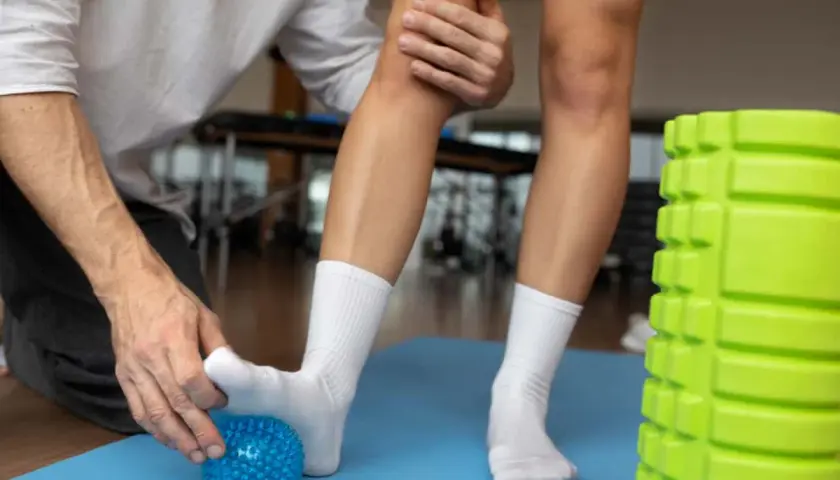 Rehabilitacja stawu skokowego: masaż stopy niebieską piłeczką, pomoc terapeuty.