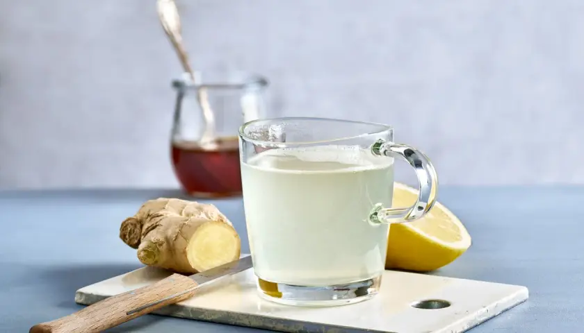 Ingwer Zitrone Tee selber machen: Ein Glas frisch aufgebrühter Tee mit Zitrone und Ingwer, daneben frischer Ingwer, Zitrone und ein Glas Honig.