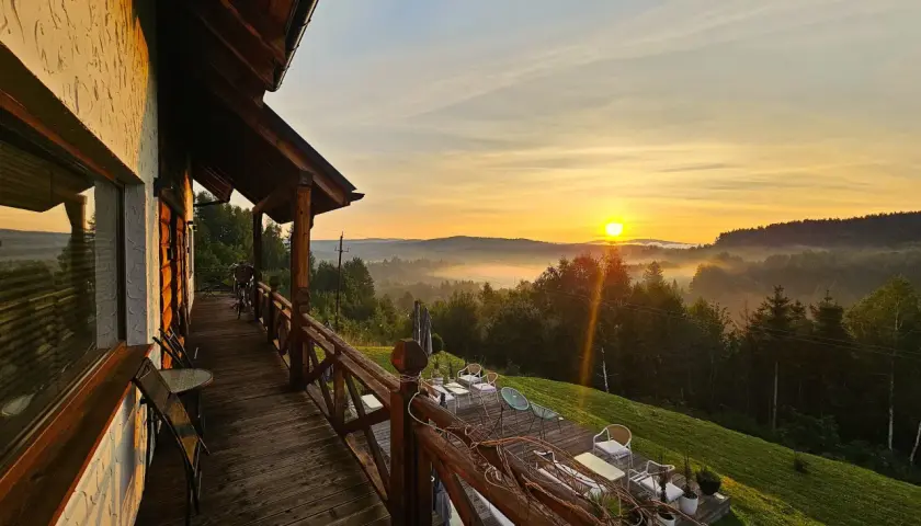 Drewniany taras z widokiem na mgliste Bieszczady o wschodzie słońca.