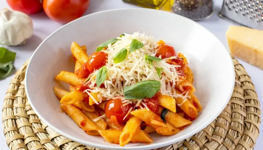 Un plato de macarrones a la napolitana, con salsa de tomate, tomates cherry, albahaca fresca y queso rallado.