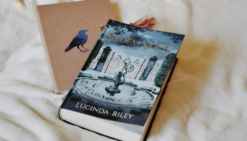 Książka "Siedem Sióstr" Lucindy Riley na tle okładki z ptakiem.