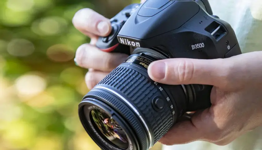 Mani che impugnano una Nikon D3500 con obiettivo 18-55mm. Dettagli sulla nikon d3500 scheda tecnica.