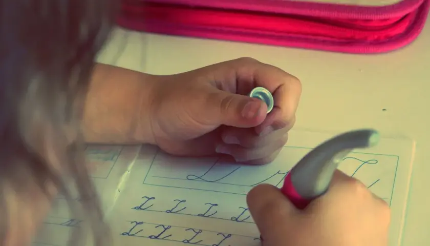 Niño/a practicando caligrafía en un cuaderno con letras cursivas.