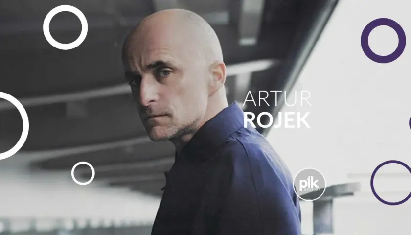 Artur Rojek, znany z energetycznych koncertów, na tle miejskiego krajobrazu.