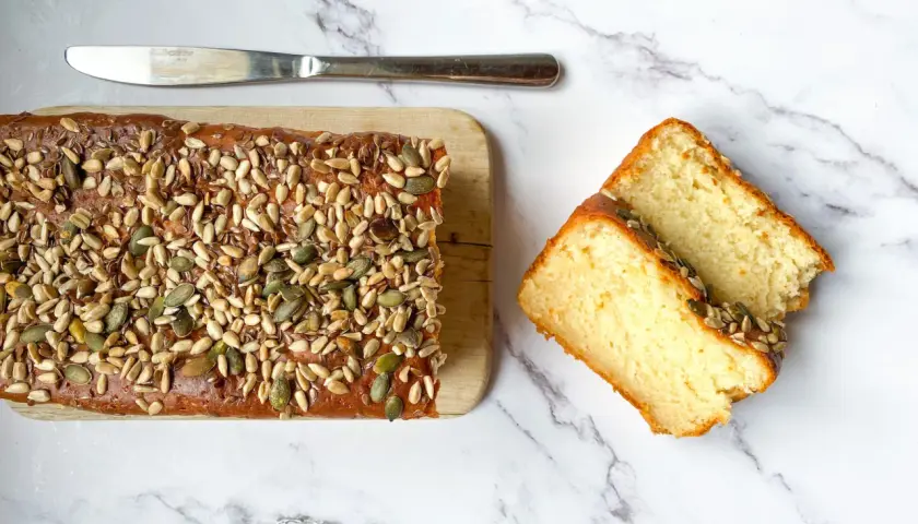 Plumcake senza uova, soffice e dorato, ricoperto di semi misti. Due fette tagliate mostrano la sua morbidezza.