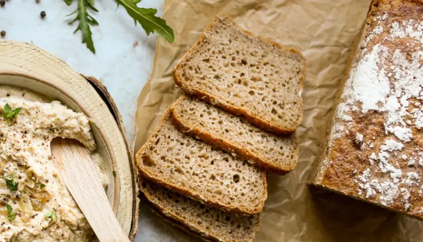 Chleb żytni, pokrojony w kromki, obok miski z pastą. Czy żyto ma gluten? Tak, żytnie pieczywo zawiera gluten.