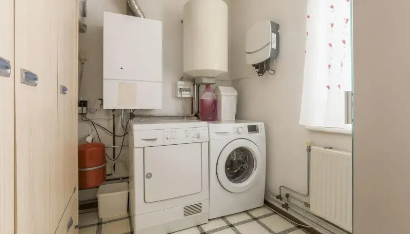 Pomieszczenie gospodarcze z pralką, suszarką, bojlerem i szafą.