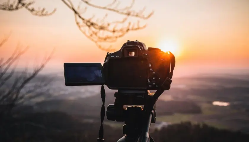 Aparat fotograficzny na statywie, gotowy do uchwycenia zachodzącego słońca nad doliną. Solidna podstawa aparatu zapewnia stabilność.