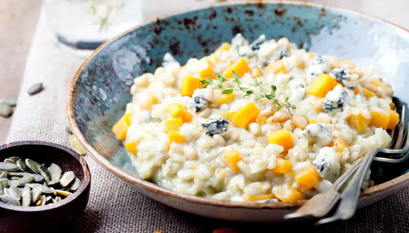 Cremiges Kürbis-Risotto mit Blauschimmelkäse und Pinienkernen. Ein Glas Wasser steht bereit, perfekt zum Genießen dieses Risotto, welcher Wein passt wohl dazu?