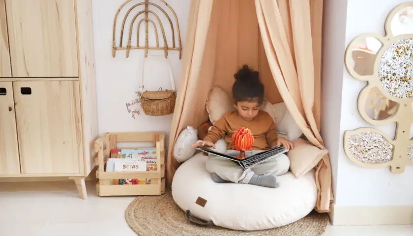 Niña en un acogedor montessori rincón de lectura niños, absorta en un libro pop-up.