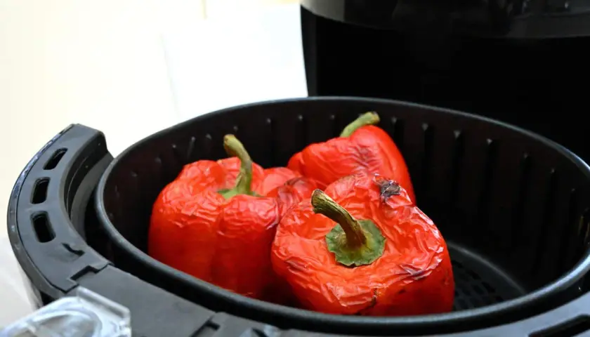 Peperoni rossi interi cotti nella friggitrice ad aria, con la buccia leggermente raggrinzita e qualche macchia scura.