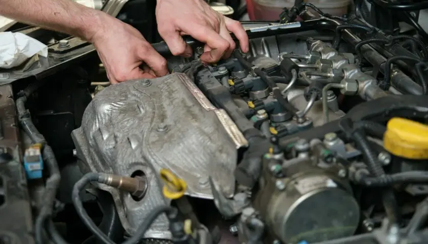 Mechanik pracuje przy silniku, sprawdzając czujnik położenia wałka rozrządu. Objawy awarii mogą być różne, od nierównej pracy po problemy z odpaleniem.