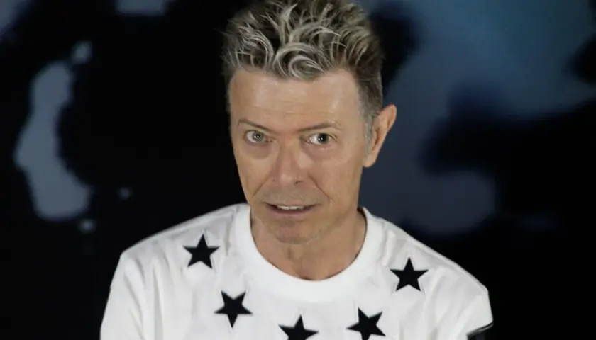 Ikoniczny David Bowie w 2016 roku, w białej koszulce w czarne gwiazdy, z charakterystyczną fryzurą.